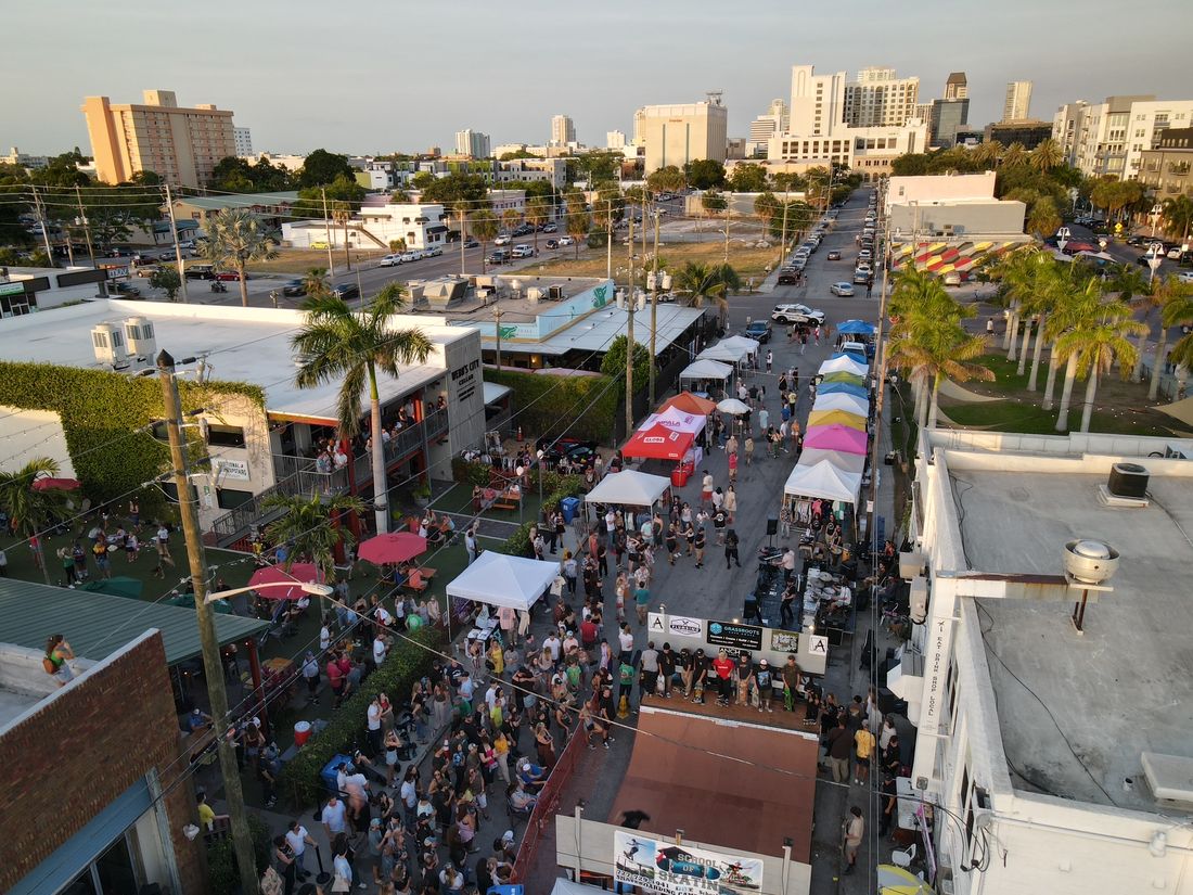 Aerial view of the Lemonade Stand Market in downtown St. Petersburg — vendor tents, crowds, live music, and the city skyline beyond.